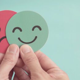 Hands holding sad face hiding behind happy face.
