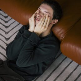 Man rubbing eyes while reclining on sofa at home.